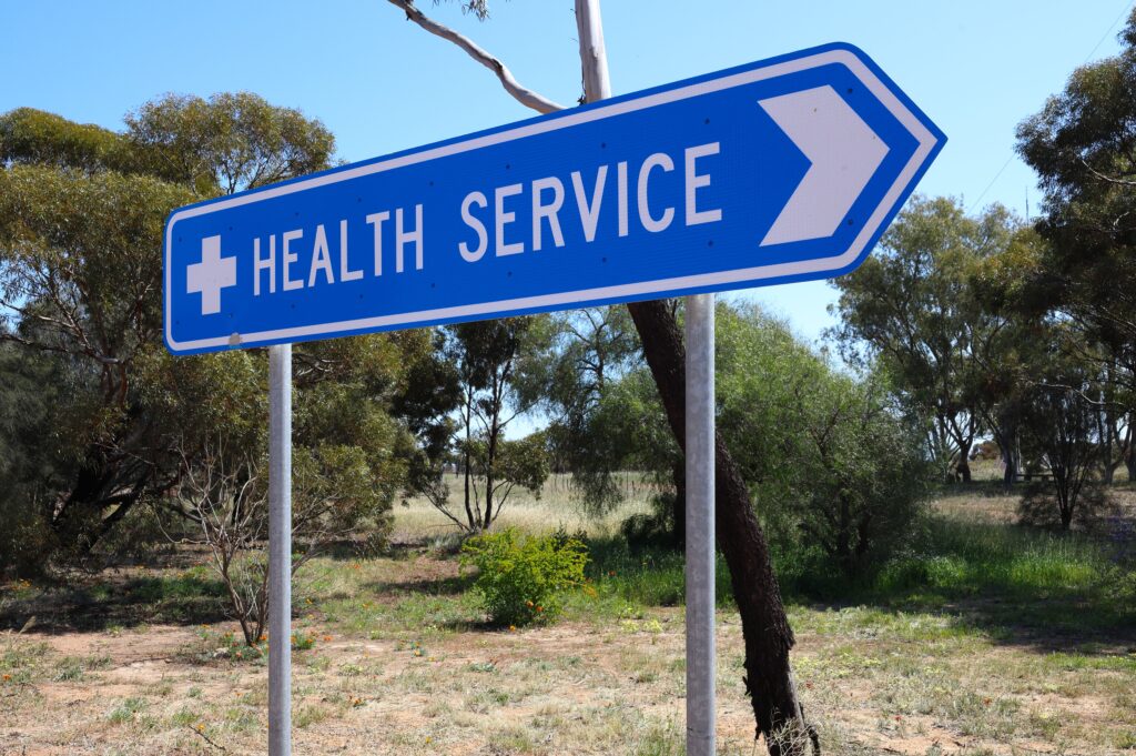 blue arrow sign that says "health service" on it next to trees in the middle of nowhere, showing reduced access to care
